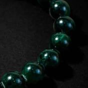Close-up of a high-quality dark green jade or obsidian bead bracelet on a black background, highlighting the smooth texture and subtle light reflections on each bead.